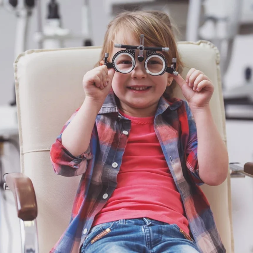 Criança em cadeira na clínica de oftalmologia infantil, com instrumento no rosto e feliz